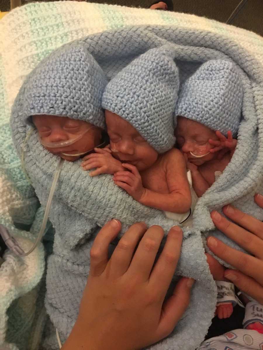 Close up of three triplet newborns sleeping in blue knit blanket with matching hats