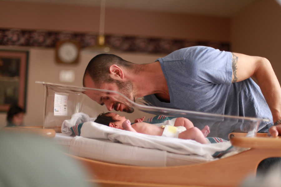 Father leans over newborn daughter to give her a kiss on forehead 