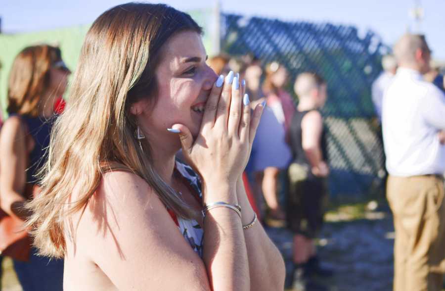 Wife smiles holding hands to her face at return of soldier husband