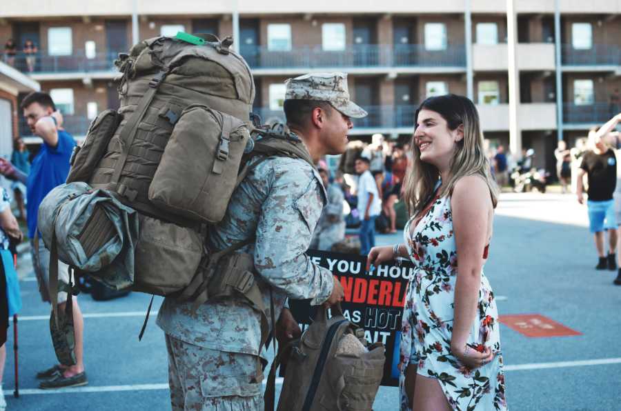 Army husband in camouflage uniform smiling at wife in parking lot