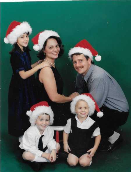 Husband and wife posing with three toddler children who are all wearing Santa hats