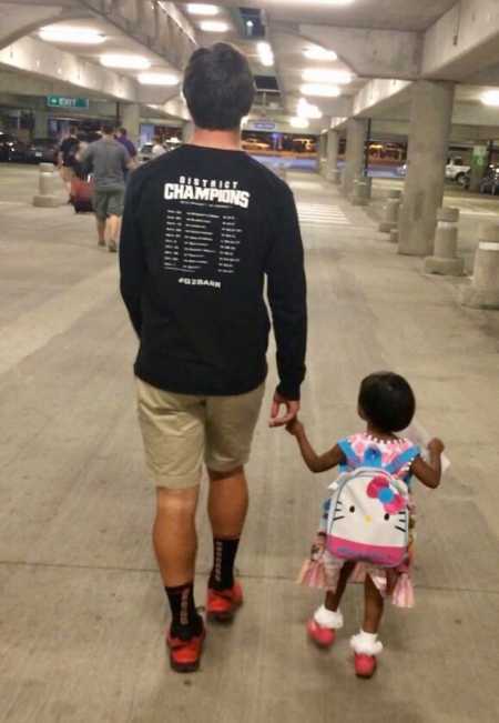 Teen boy holds hand of adopted toddler sister in parking garage