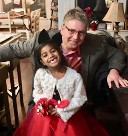 Father smiles while kneeling behind adopted daughter dressed for daddy daughter dance