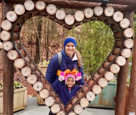 Mother smiles while standing behind adopted daughter inside of heart made out of wood logs