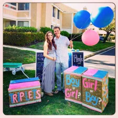 Husband and wife who battled with fertility hold pink and blue balloons and boxes decorated for gender reveal