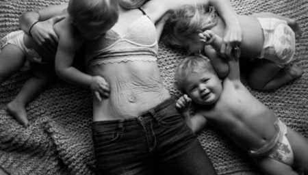 Mother lays on floor without shirt on with her triplets in diapers