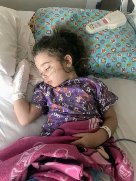 Young girl with aspiration pneumonia sleeping in hospital bed with cast on hand and tubes up her nose