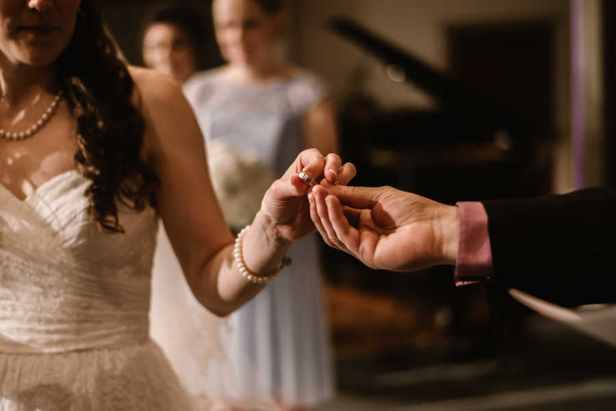 Hand holding grooms ring while bride grabs it