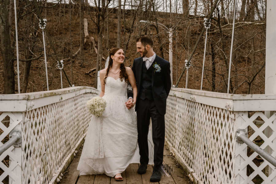 Bride and groom smile hand in hand while walking on bridge