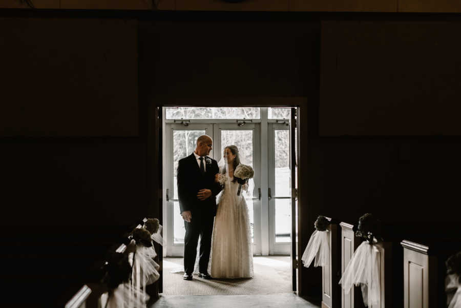 Bride stands arm in arm with father who who is about to give her away