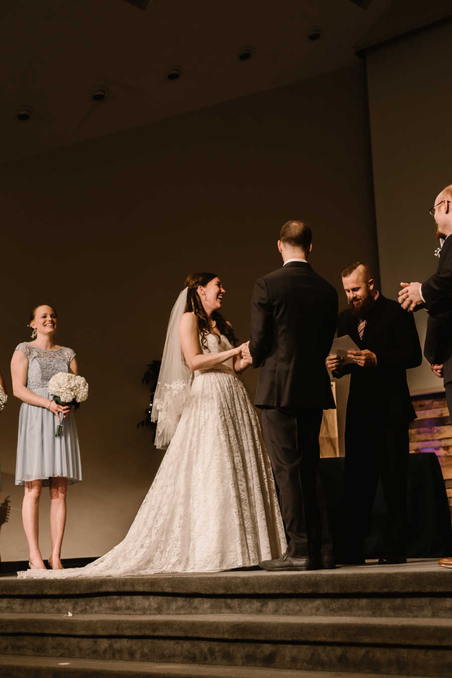 Bride and groom standing hand in hand at altar laughing at officiant