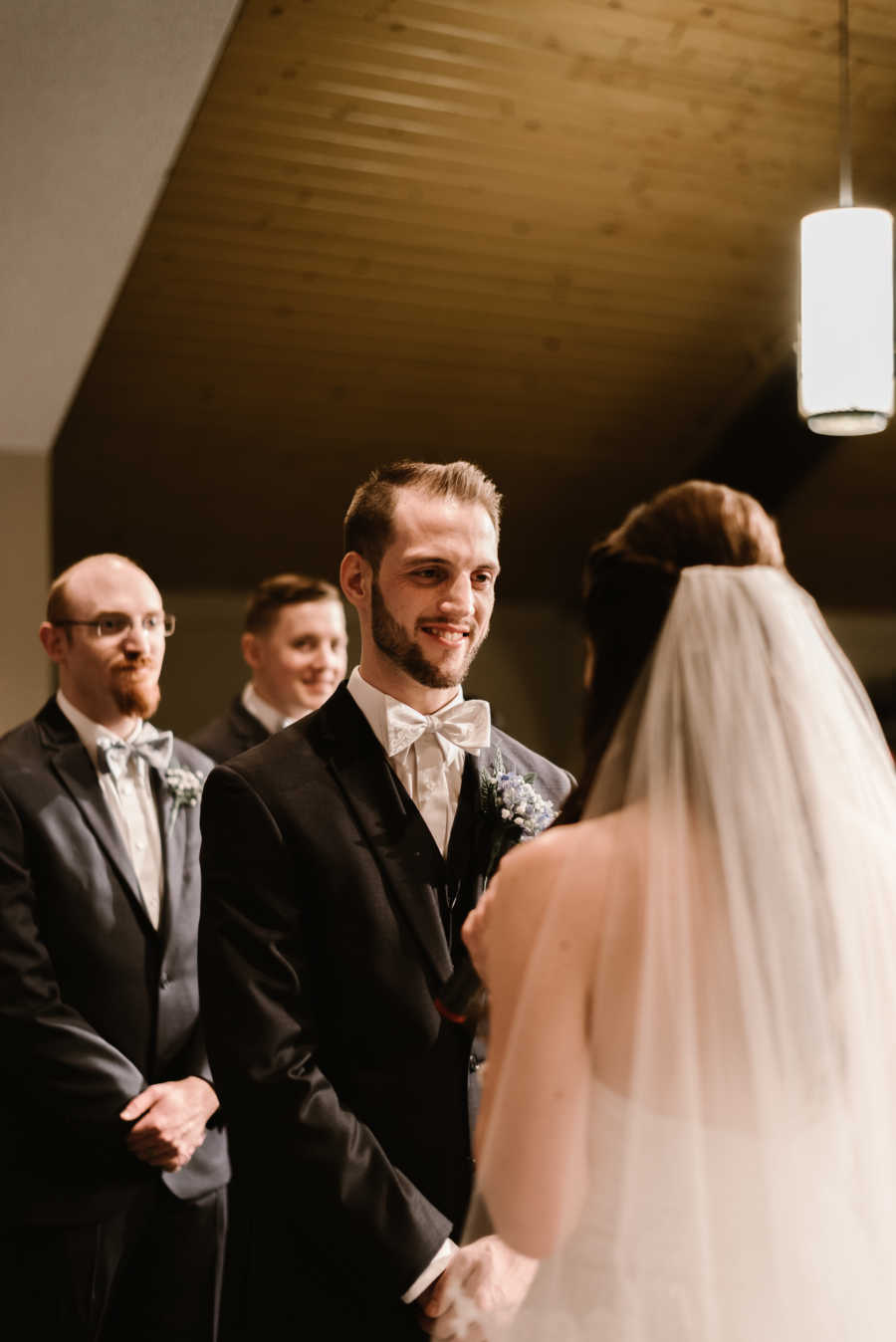 Groom stands smiling at bride at altar