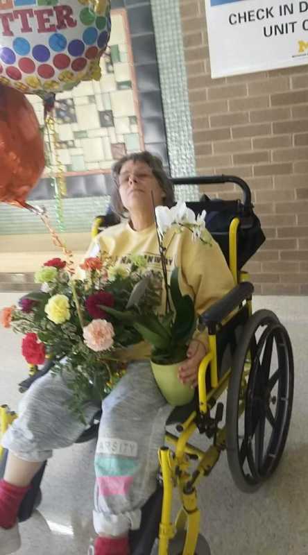 Mother sitting in wheel chair with flowers in her lap after kidney surgery that was donated by son