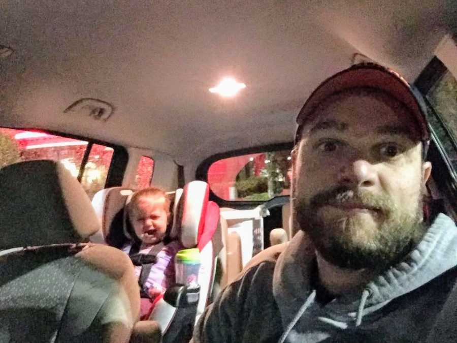 Father takes selfie in car with toddler daughter in back seat crying in restaurant parking lot