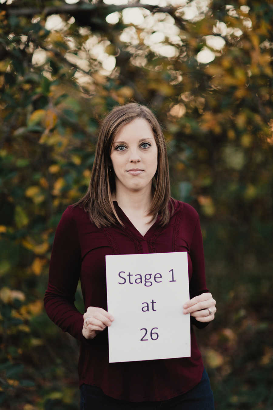 Young mother with breast cancer holds up sign saying, "stage 1 at 26"