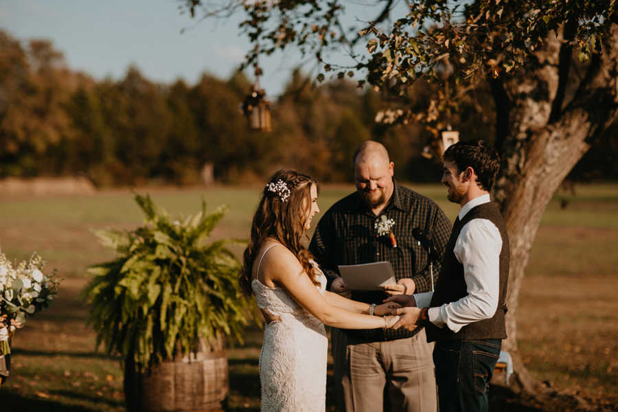 Bride and groom hold hands at altar of out door wedding with officiant