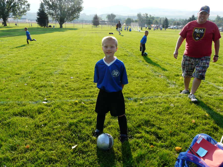 Toddler with cerebellar atrophy standing in soccer uniform with soccer ball at his feet