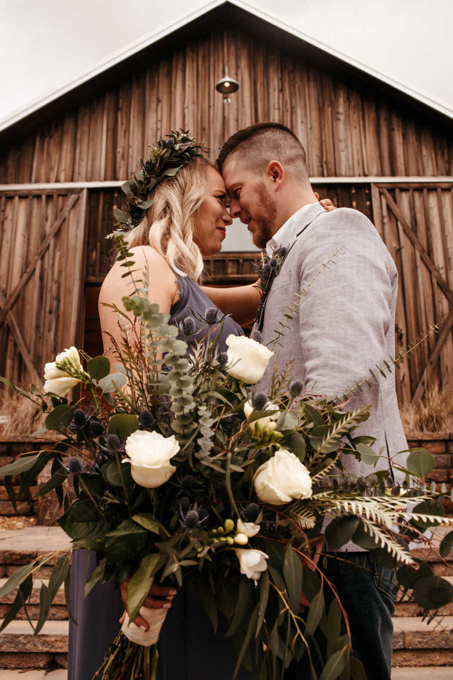 Nurse girlfriend and EMT boyfriend stand with heads touching in front of barn