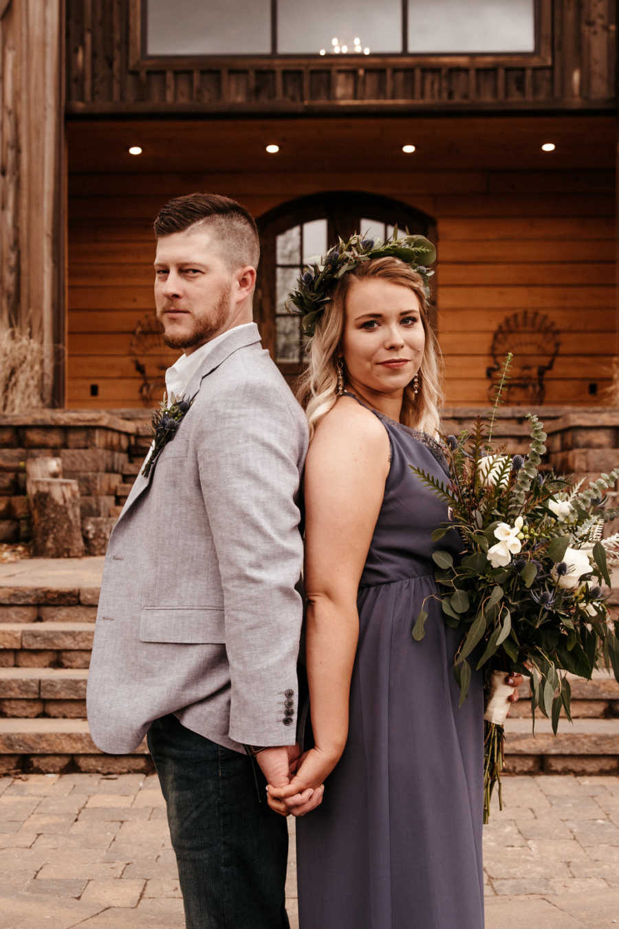 Boyfriend and girlfriend stand back to back holding hands in front of barn