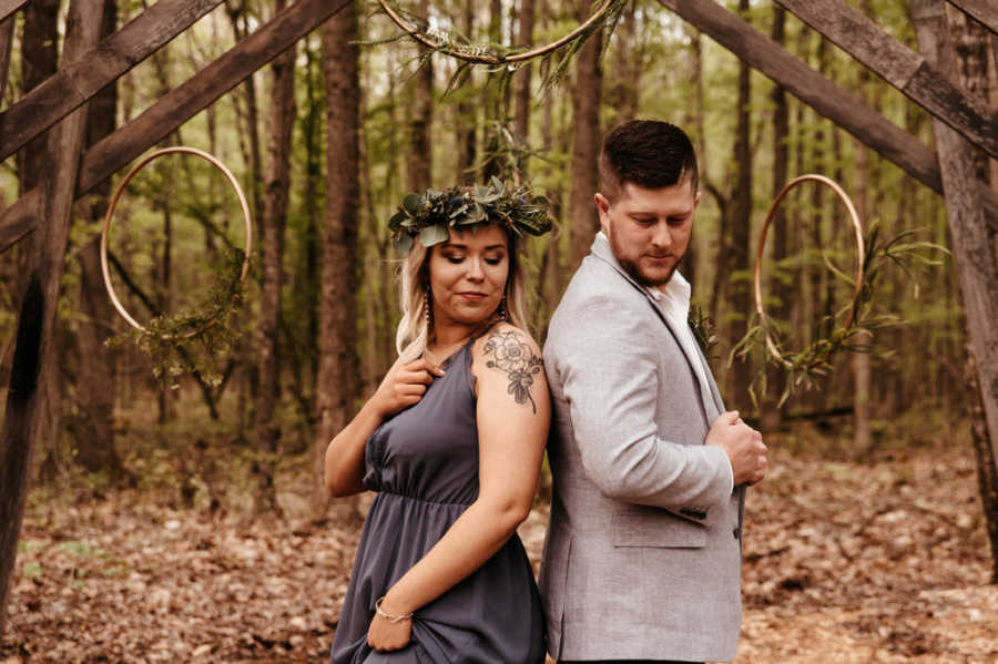 Boyfriend and girlfriend standing back to back under wooden archway in woods