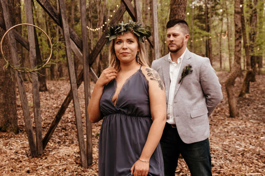 Girlfriend standing with back to boyfriend in woods as he stands with hands behind his back