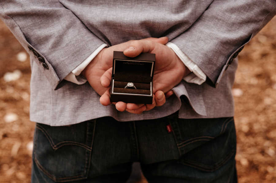 Close up of boyfriend holding box with engagement ring behind his back