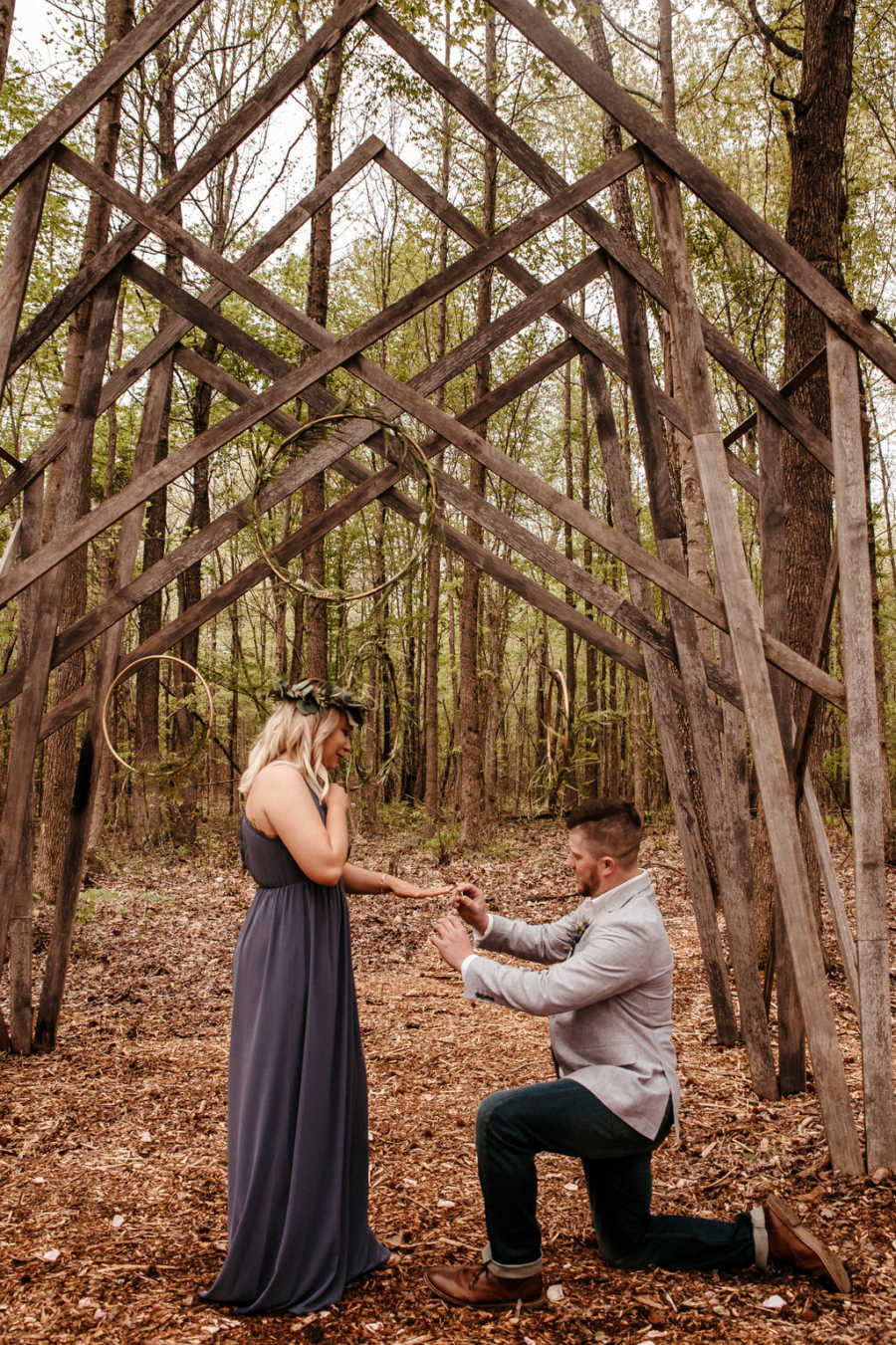 Boyfriend placing engagement ring on girlfriend as he proposes under wooden arch