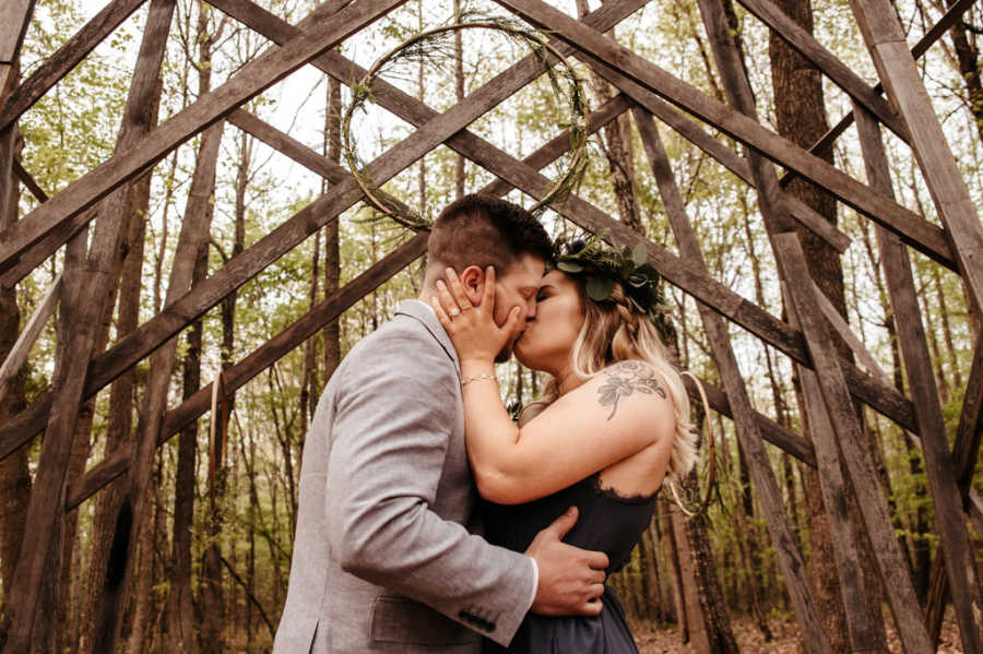 Newly engaged couple kiss under wooden archway