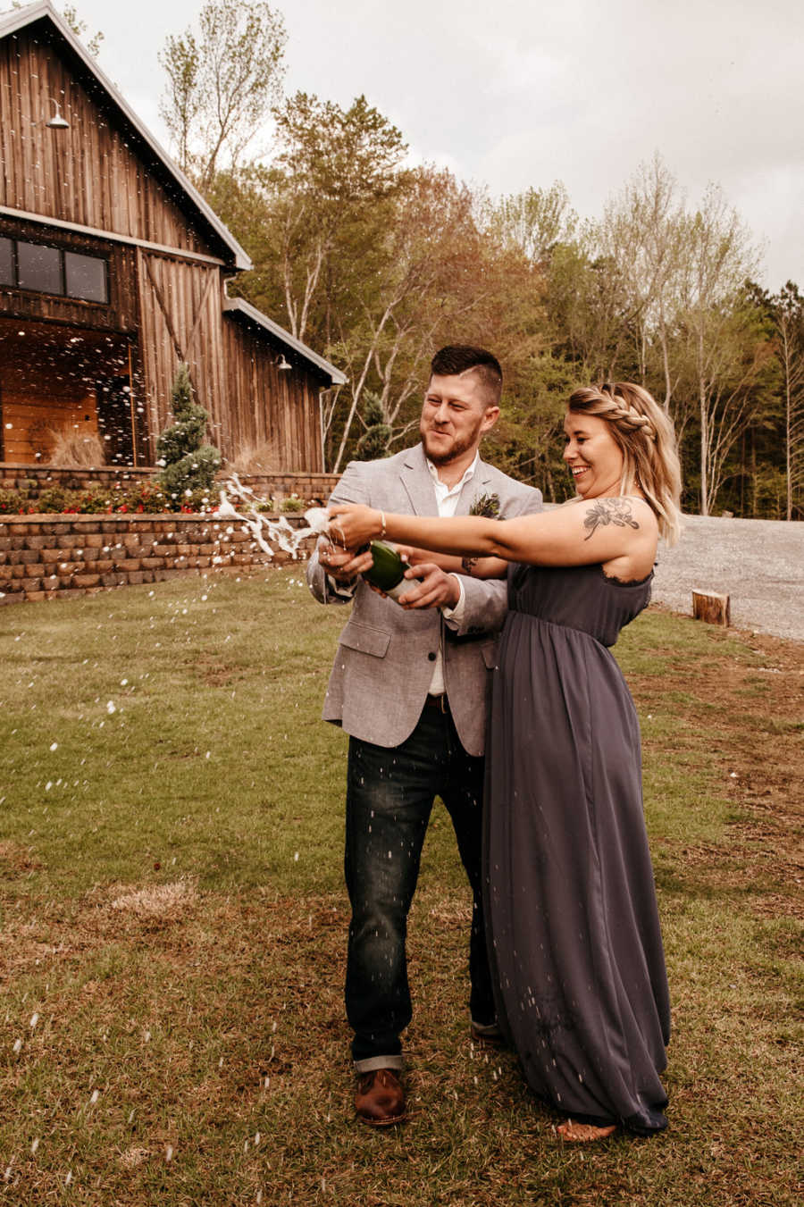 Newly engaged couple pop bottle of champagne together outside of barn