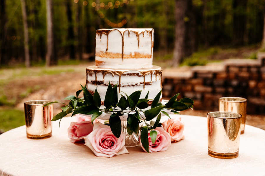 Three tiered cake on table surrounded by pink roses for celebration of engagement