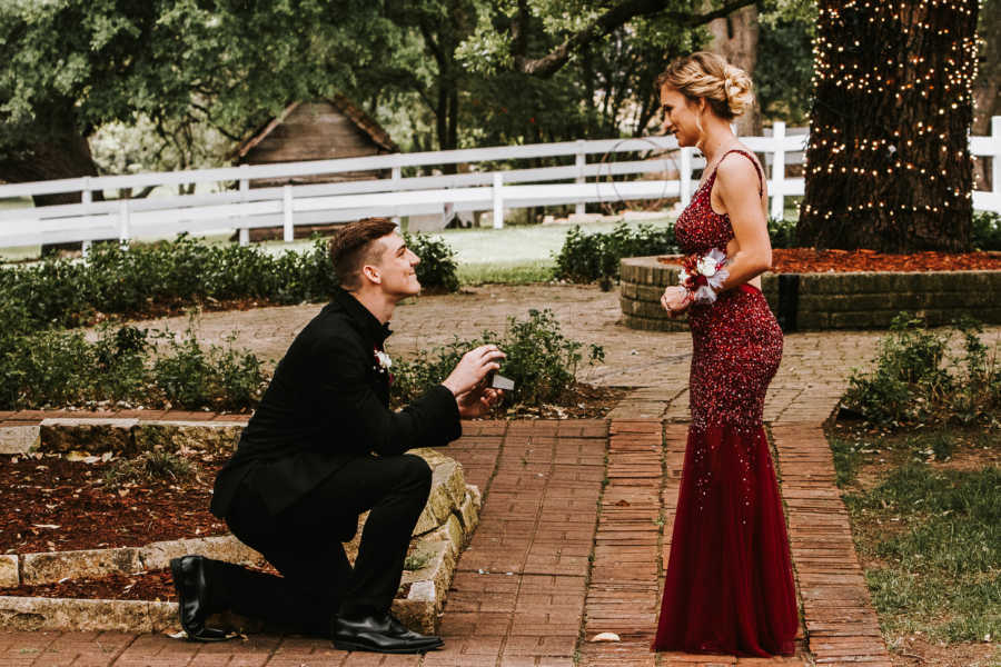 Girl in prom dress stands over boyfriend who is proposing