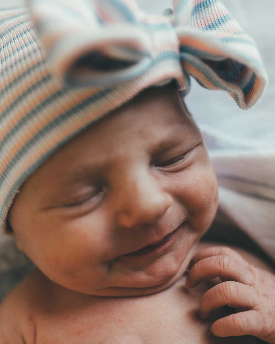 Close up of newborn conceived naturally smiling with striped hat with bow on it