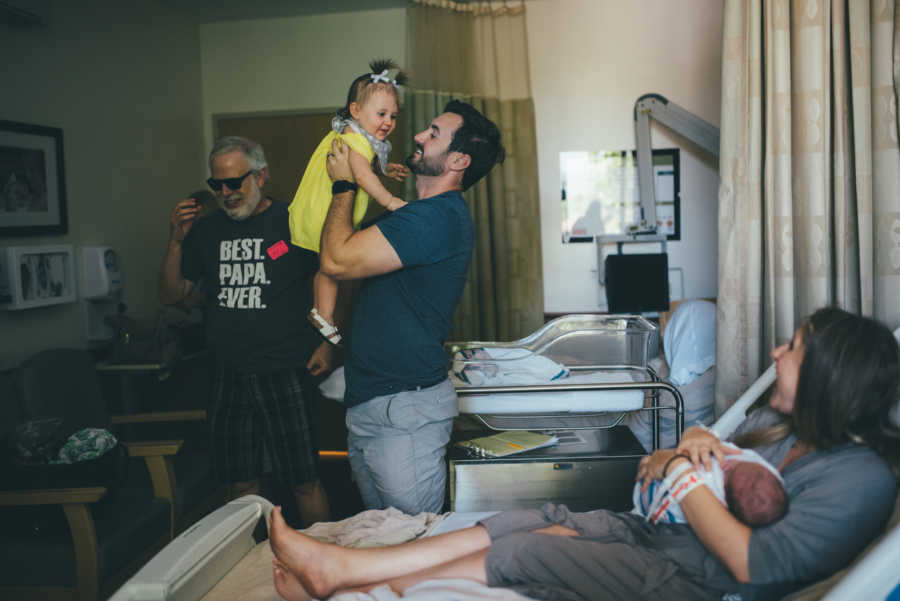 Father holds firstborn conceived through IVF beside wife who is holding natural born newborn