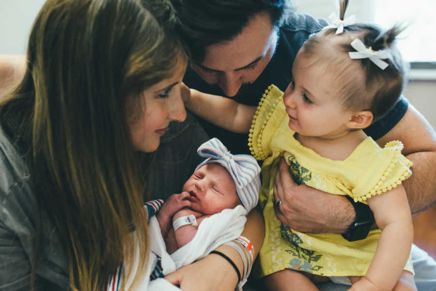Husband and wife hold newborn baby and three month old IVF daughter in their lap