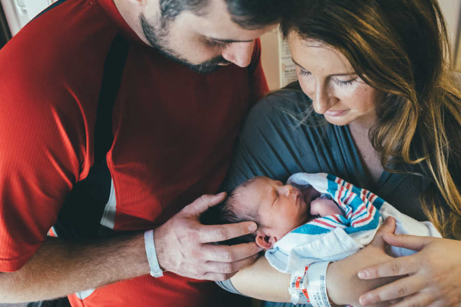 Mother holds newborn conceived naturally in her arms with her husband by her side 