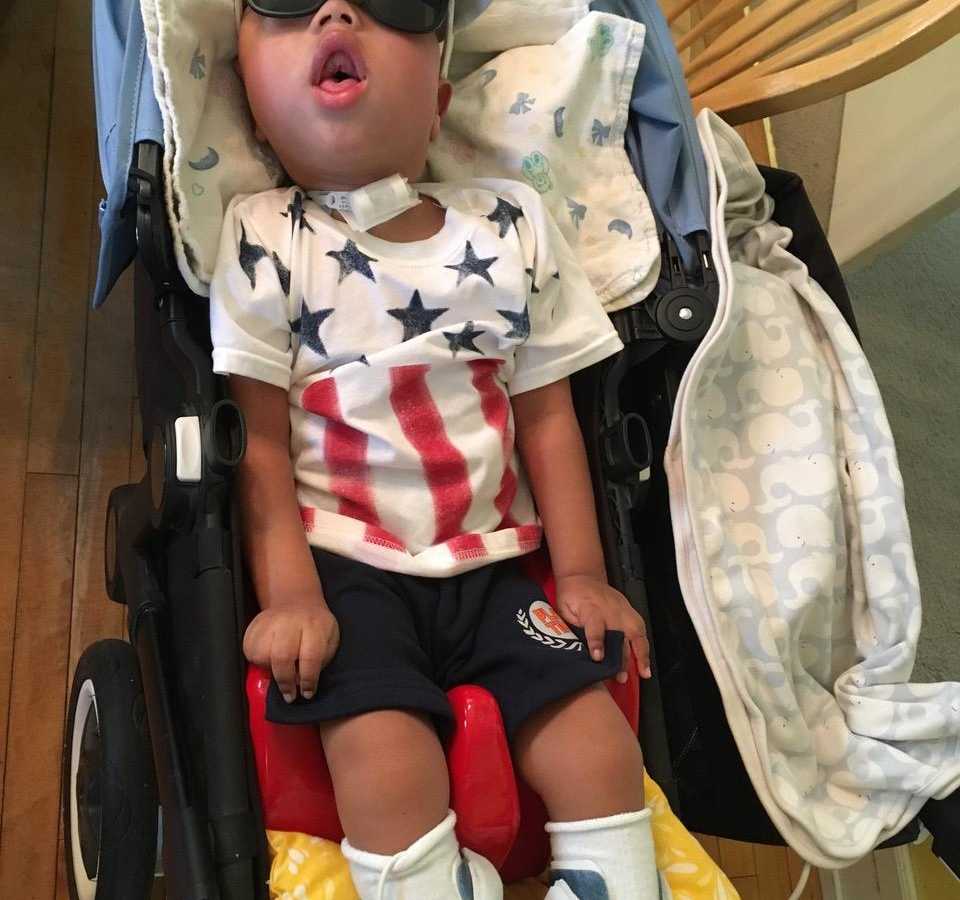 Terminally ill toddler who was adopted by woman leans back in stroller