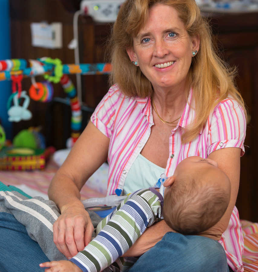 Woman smiles while holding adopted son who is terminally ill in her lap