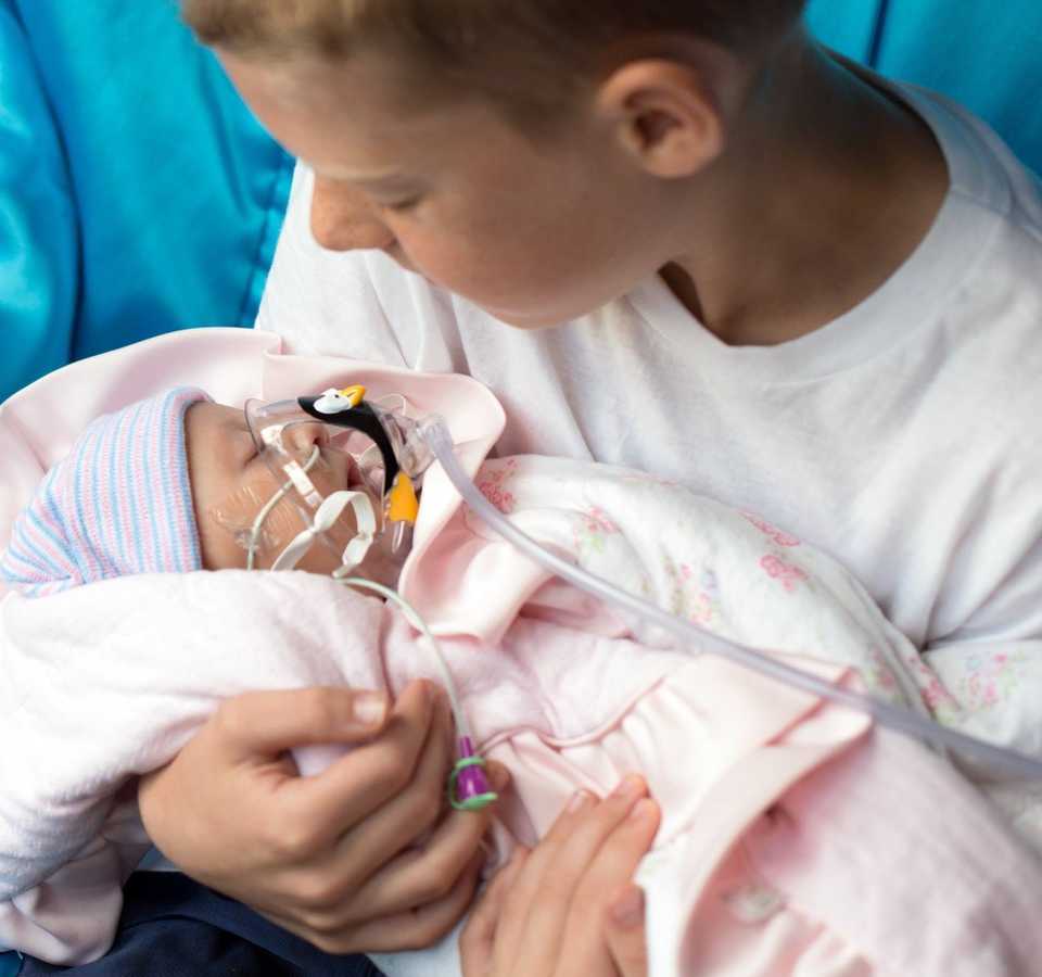 Young boy holds infant who was adopted by woman and is terminally ill