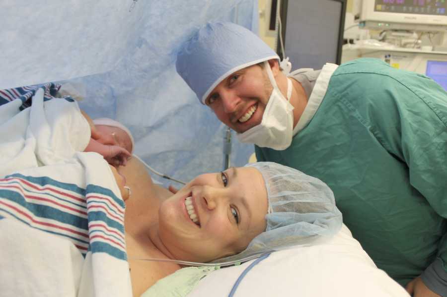 Husband and wife smile while wife holds newborn after c-section