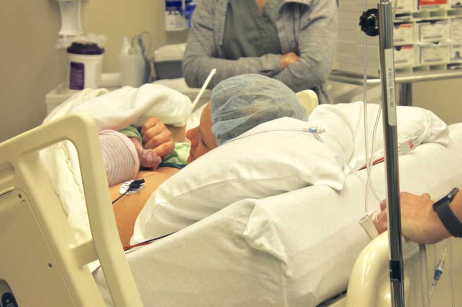 Mother laying in hospital bed after c-section holding hand of newborn