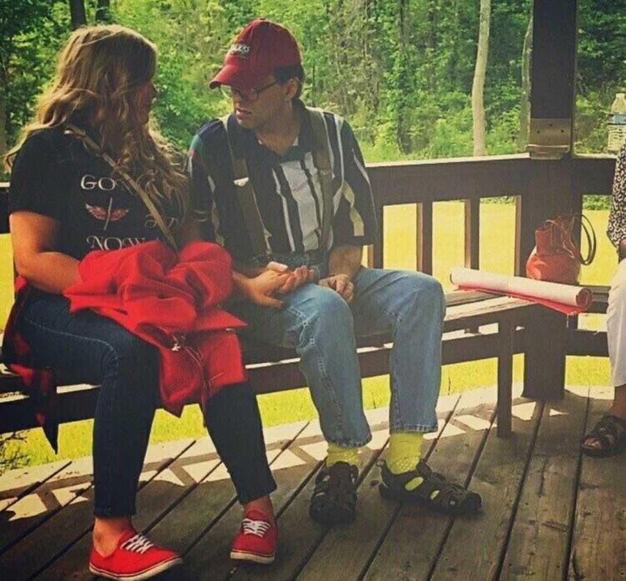 Daughter sitting with father who has parkinson's and dementia on wooden bench