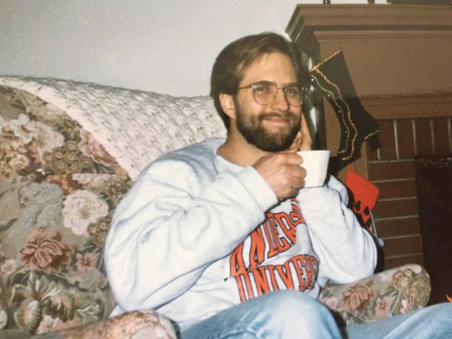 Man who will later in life suffer from dementia sitting in chair smiling and holding mug