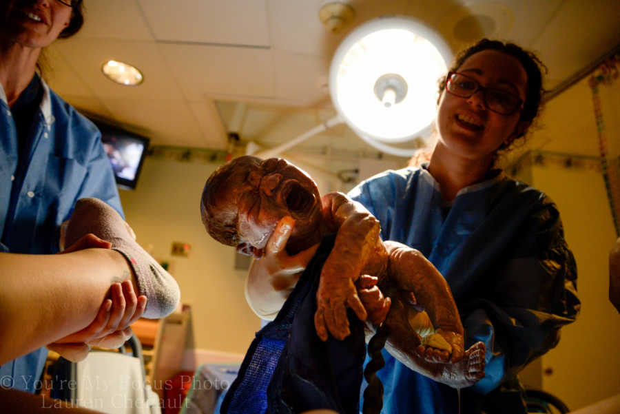 OBGYN holding newborn baby covered in blood up in air