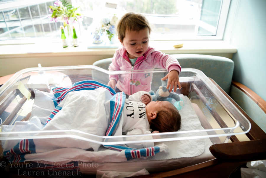 Older sister reaches over to touch newborn sibling on head