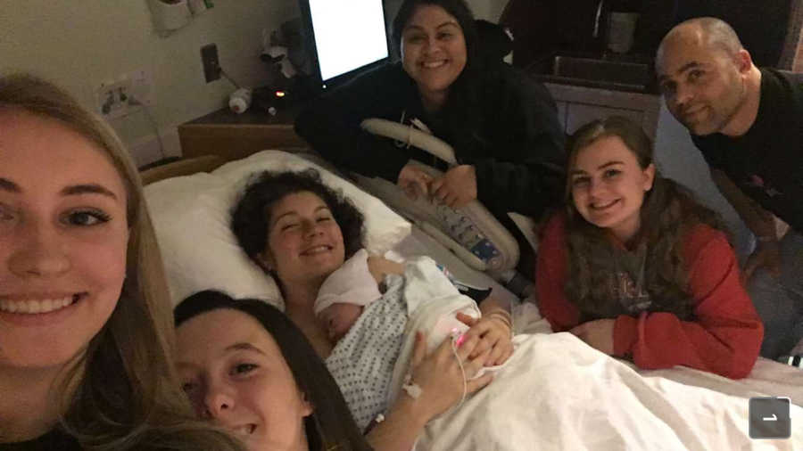 Woman who photographed herself giving birth lays in hospital bed with newborn with family at her side