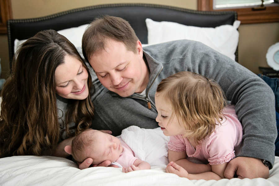 Mother and father lay on bed beside newborn and first born