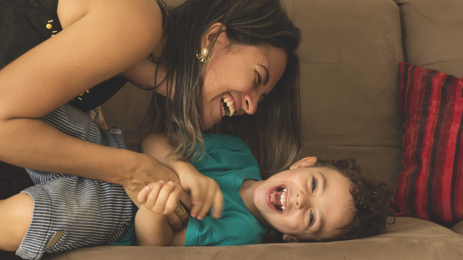mom laughing and tickling toddler lying on couch