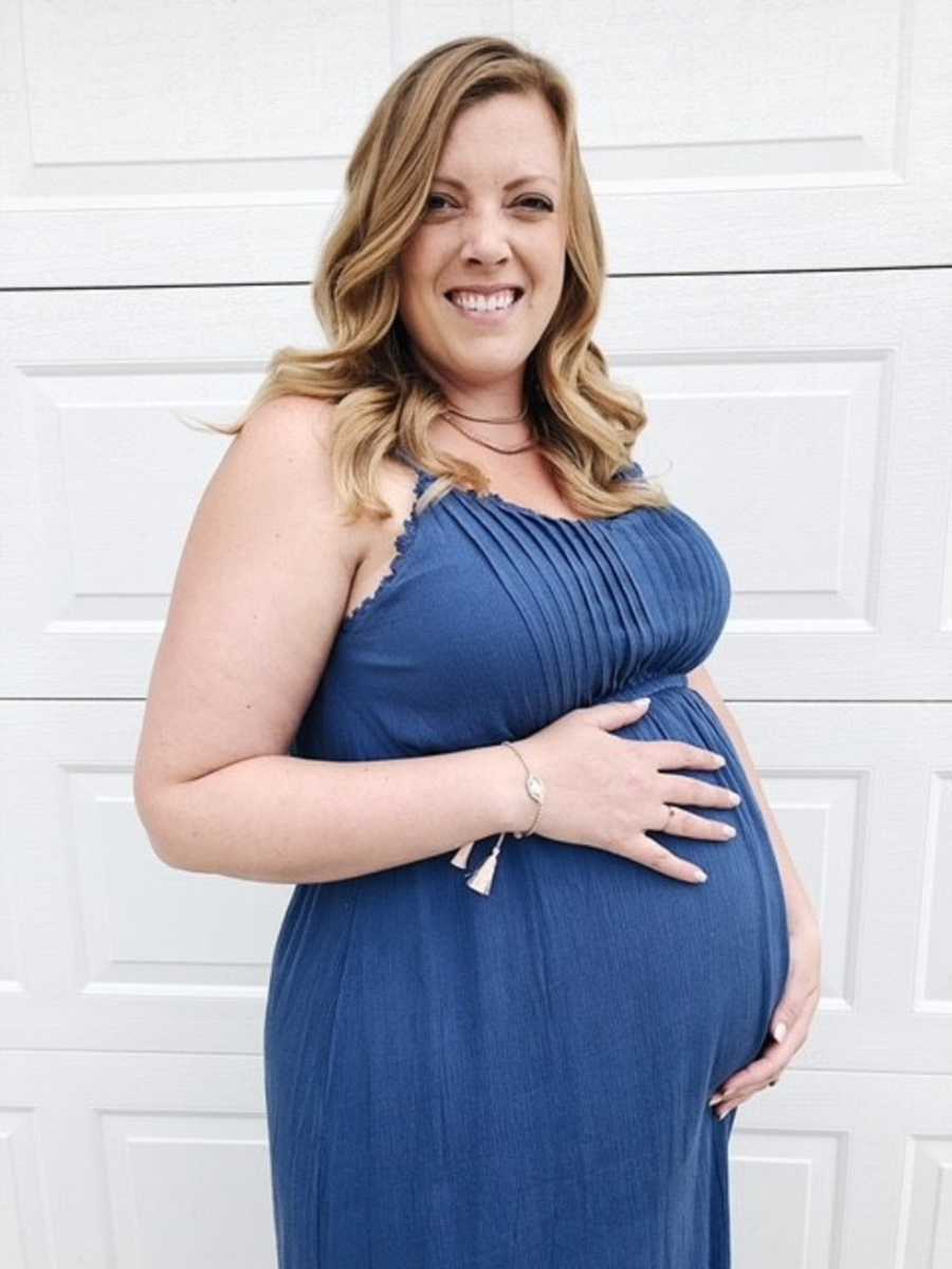 Pregnant woman who struggles with postpartum anxiety smiling while holding her stomach