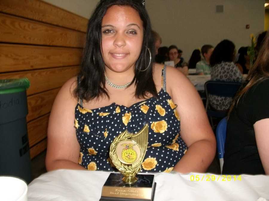 18 year old who weighed 300 pounds sitting at table with trophy in front of her