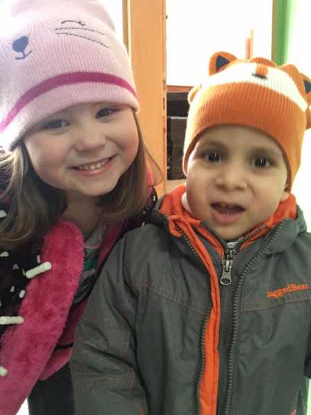 5 year old girl standing and smiling next to adopted brother who was born without an esophagus 